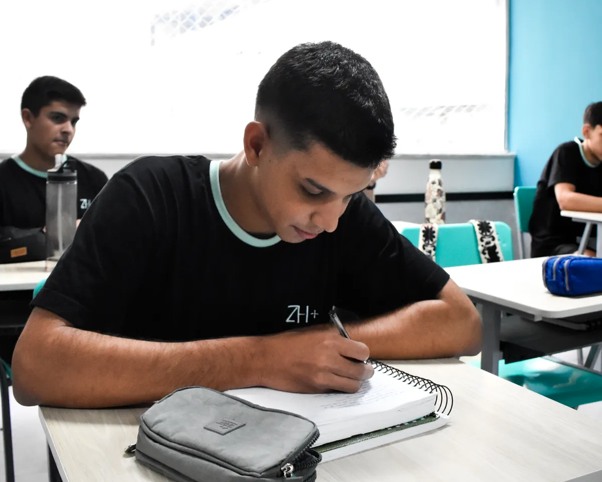 Aluno do Ensino Médio do ZH+ escrevendo no caderno durante a aula